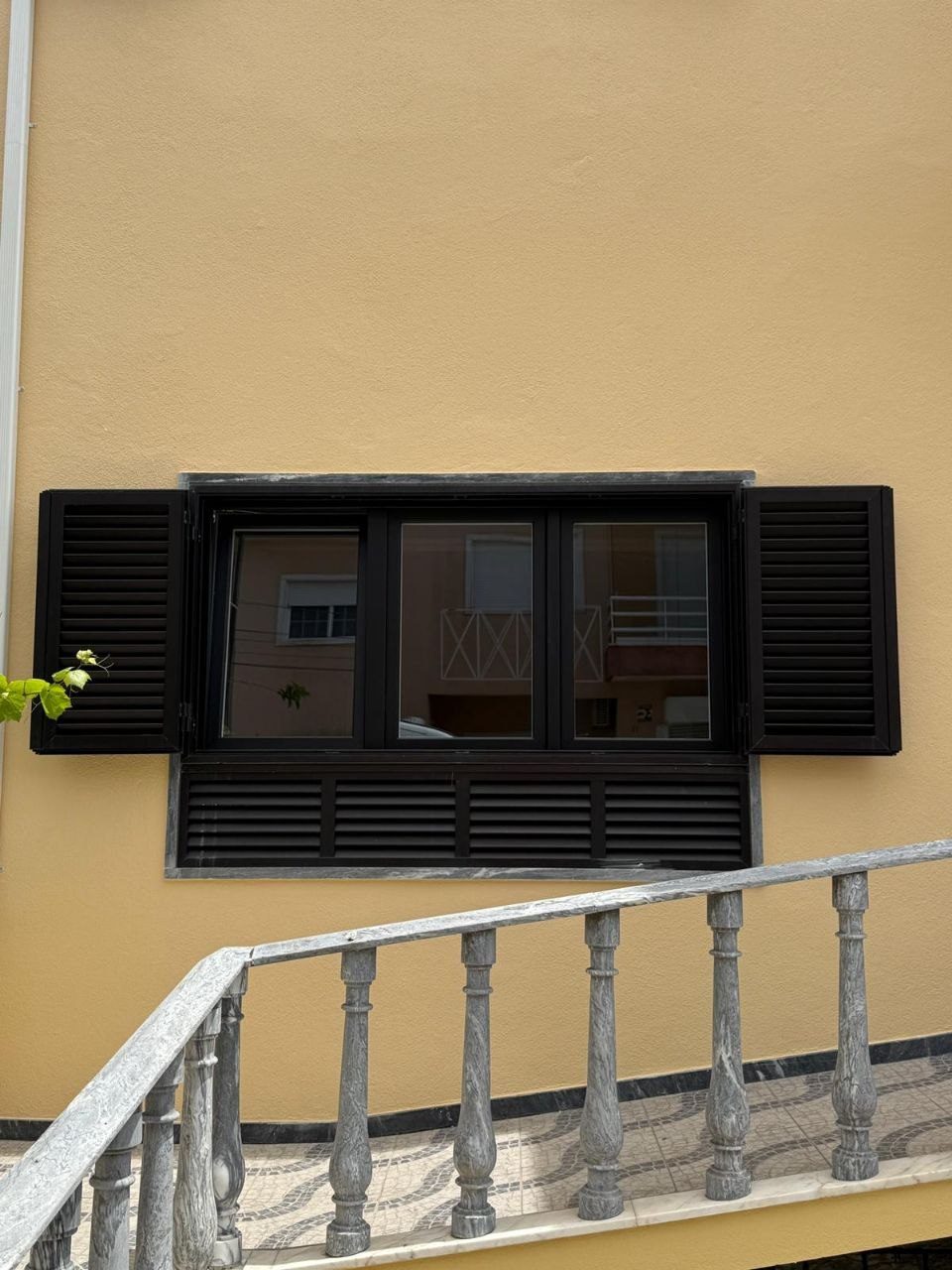 Janela em alumínio lacado preto com portadas de lâminas e painel de ventilação, vista do exterior
