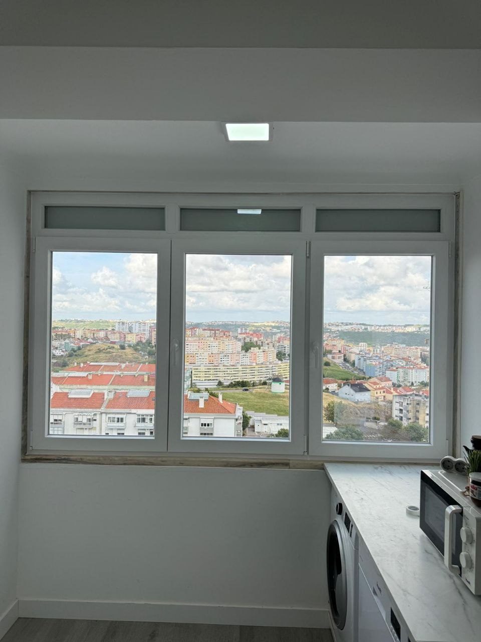 Conjunto de três folhas com bandeira fixa superior em vidro fosco, numa zona de lavandaria com vista sobre a cidade