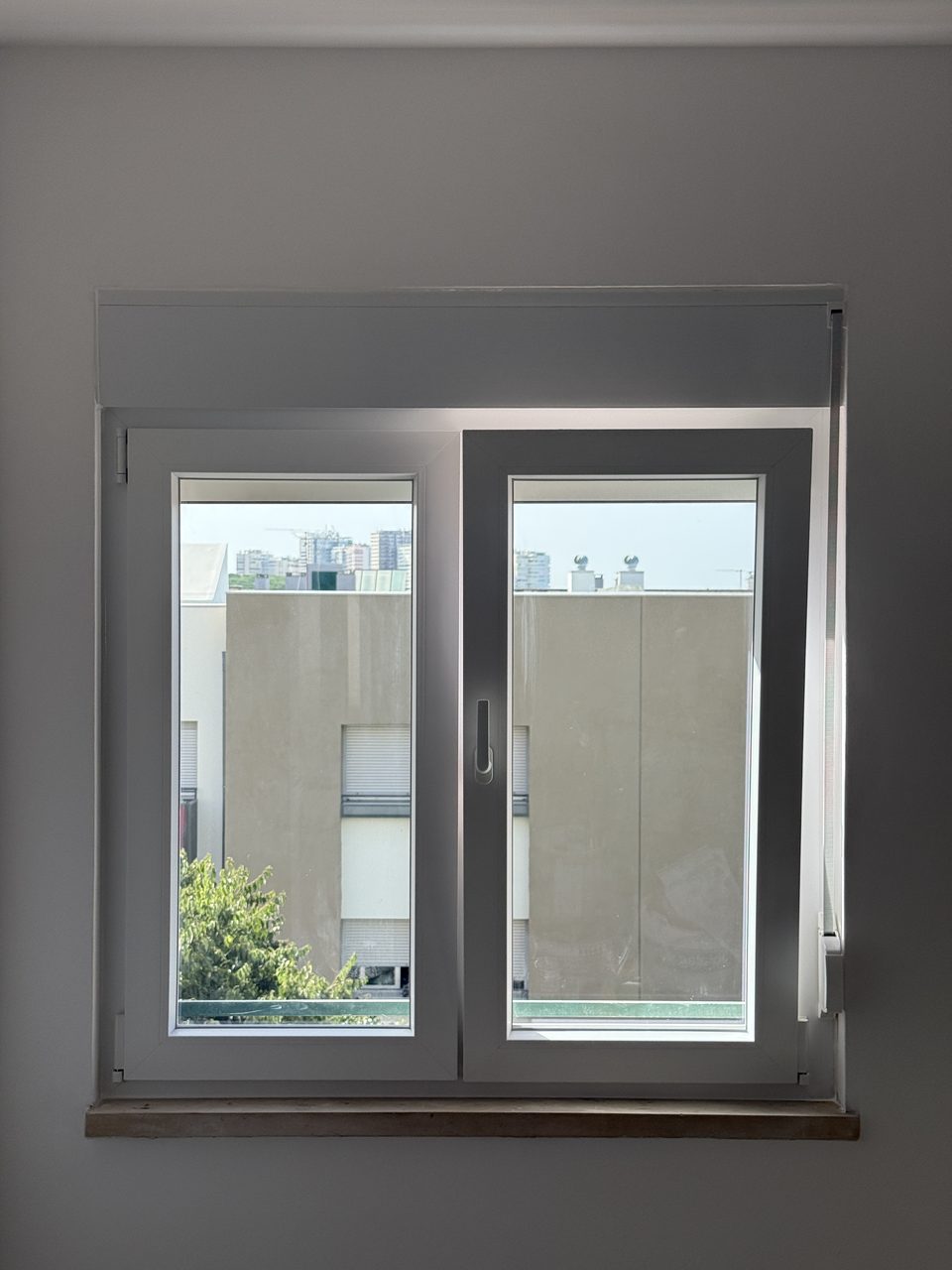 Janela oscilo-batente de duas folhas em PVC branco, com a caixa e a guia do estore visíveis