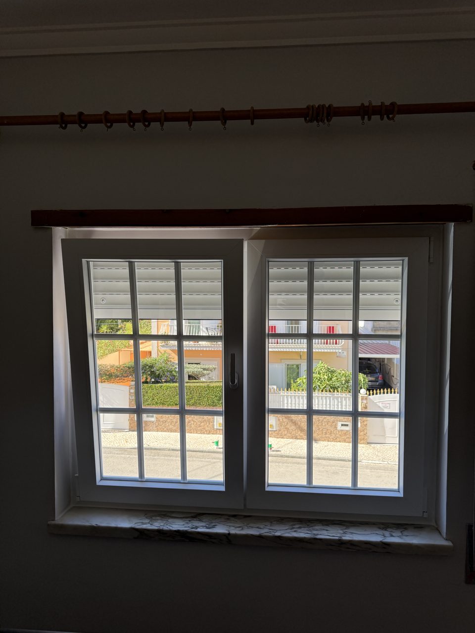 Janela de duas folhas em PVC branco com quadrícula, com o estore exterior meio descido