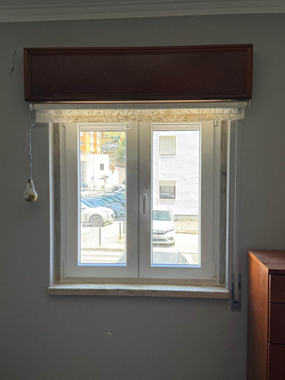 Janela de duas folhas em PVC branco num quarto, com a sanefa de madeira e o estore exterior originais mantidos