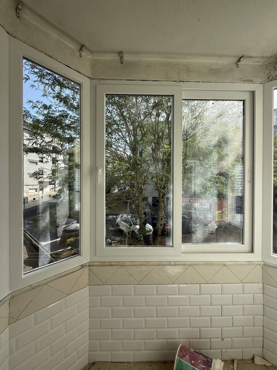 Marquise de canto em PVC branco sobre parede de azulejo, com vista para as árvores