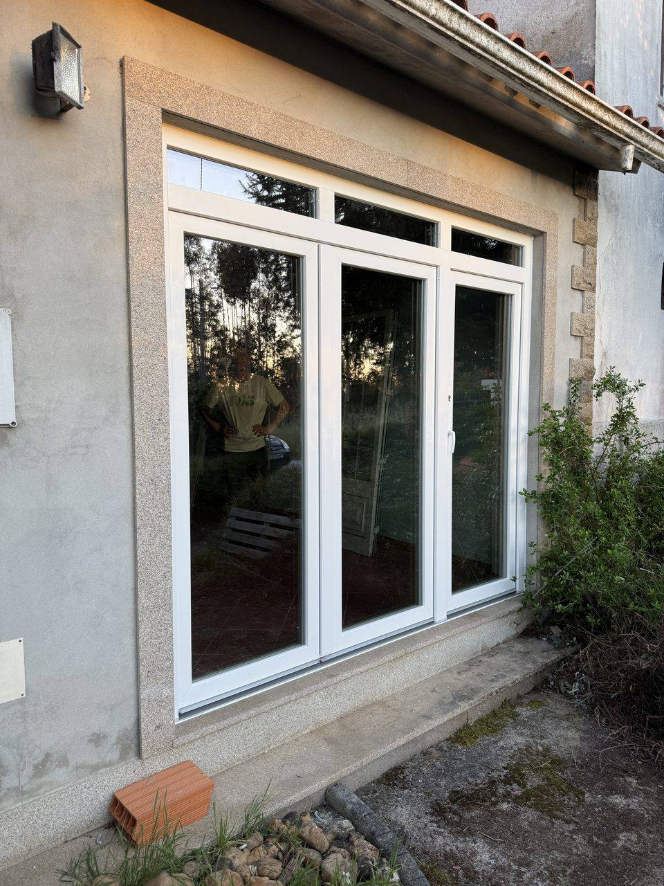Porta-janela de três folhas com bandeiras superiores em PVC branco, numa moradia com moldura de granito, vista do exterior