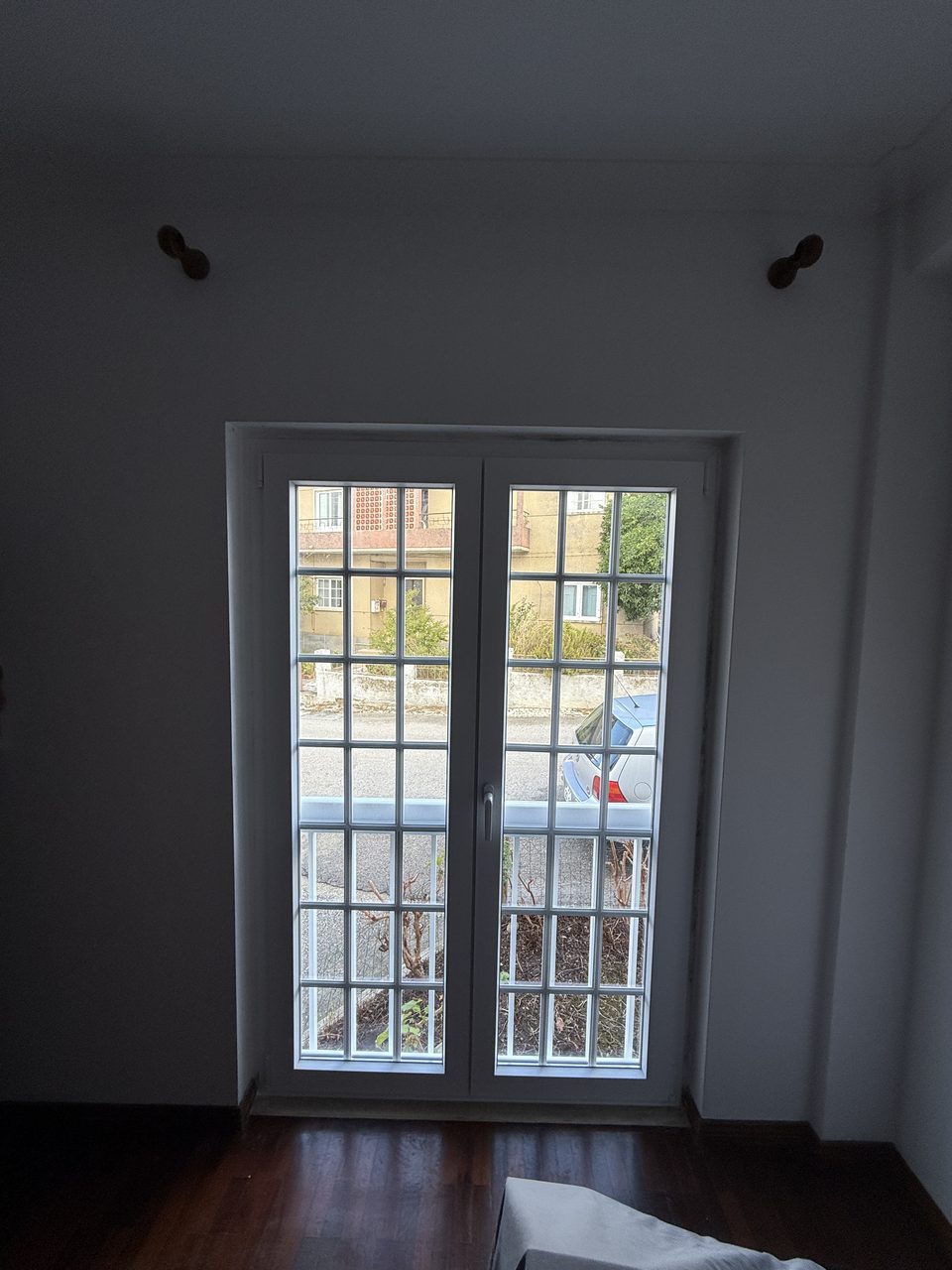 Porta-janela de duas folhas em PVC branco com quadrícula, numa sala com chão de madeira