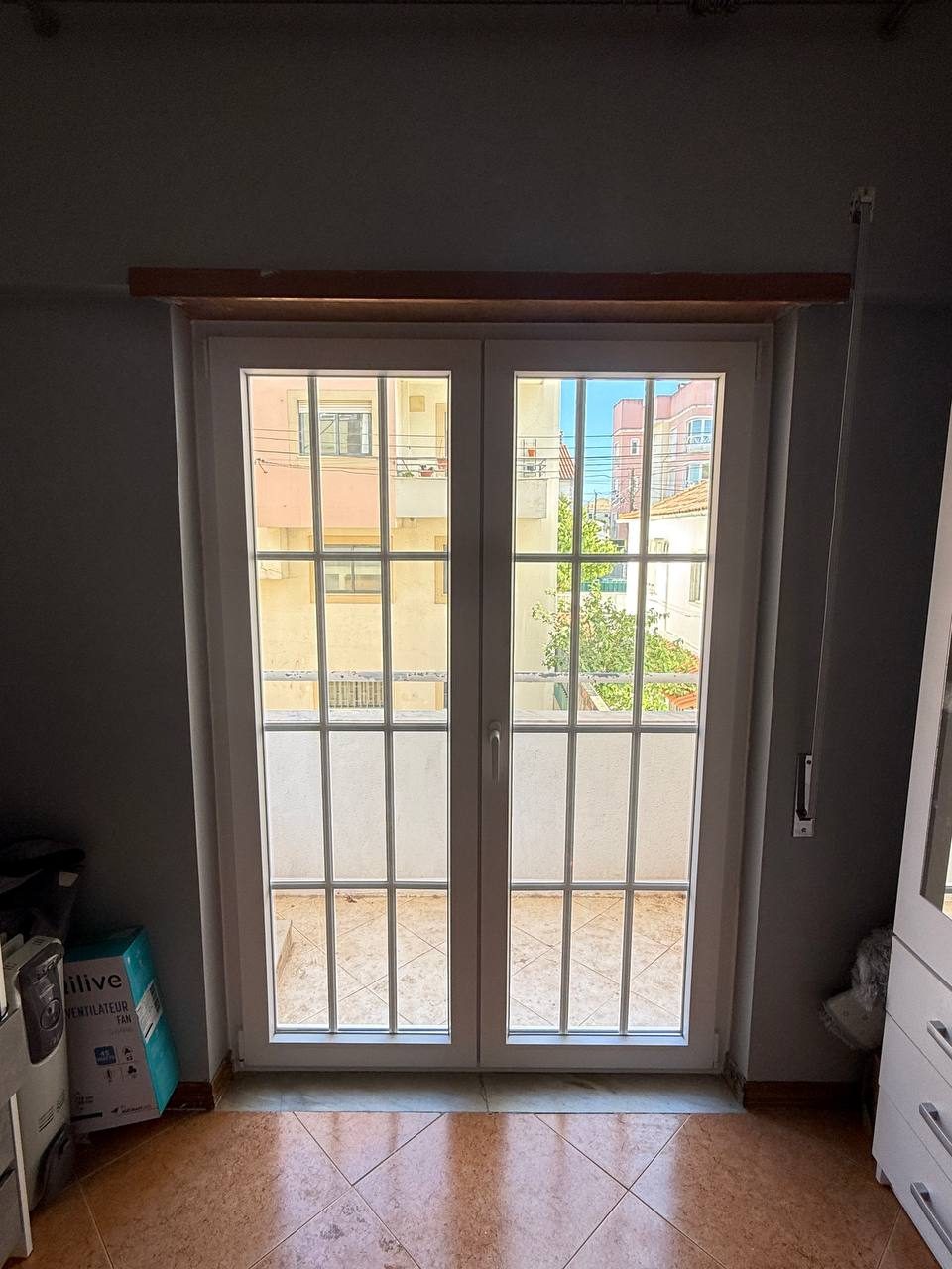 Porta-janela de duas folhas em PVC branco com quadrícula, de acesso à varanda