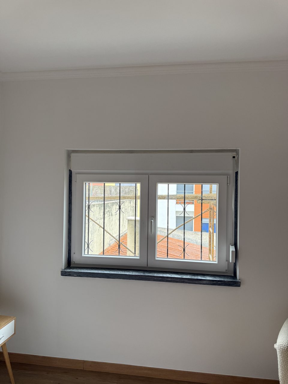 Janela de duas folhas em PVC branco num quarto, com a caixa de estore por cima