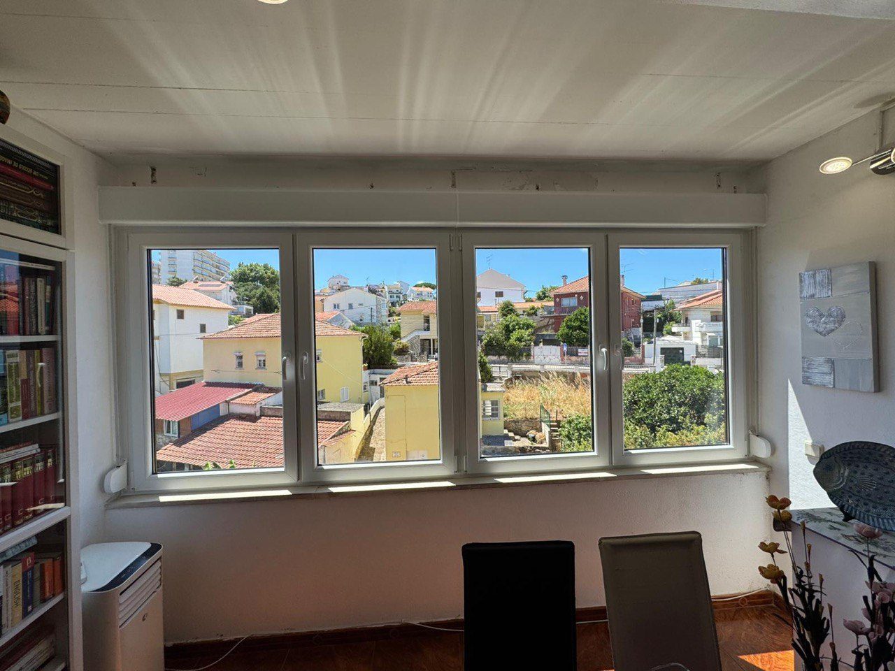 Janela de quatro folhas em PVC branco numa sala, com vista sobre os telhados
